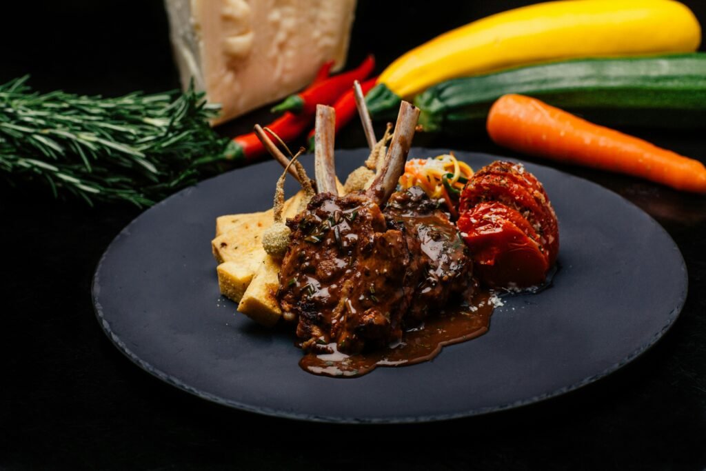 Deliciously cooked lamb chops with gravy, served with vegetables on a black plate.