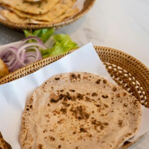 Close-up of freshly cooked Indian flatbread served in a wicker basket on a white table.