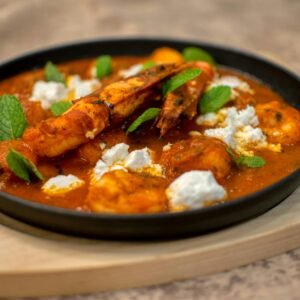 Close-up of a prawn curry garnished with cheese and fresh mint leaves, served in a black bowl.