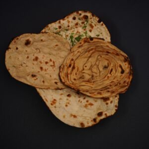 Top-down view of various Indian breads including lachha paratha and naan on a dark background.