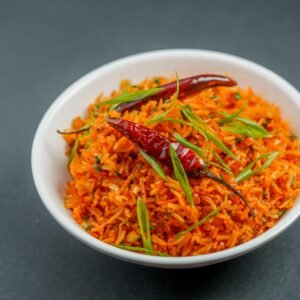 Delicious Indian rice bowl garnished with green herbs and red chilies, perfect for spice lovers.