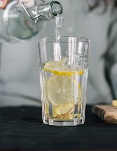 A glass of lemon water with ginger being poured for a refreshing detox drink.