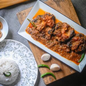 Top view of a spicy fish curry served with rice and fresh garlic on a wooden table.
