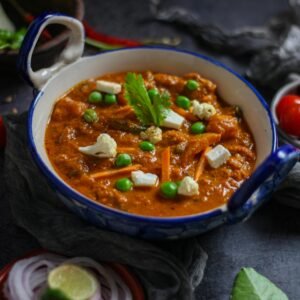 Close-up of vibrant Indian mattar paneer curry with fresh ingredients in a ceramic bowl.