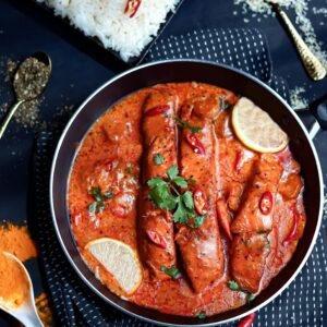 Flavorful fish curry with red sauce and rice, garnished with lemon slices and herbs.