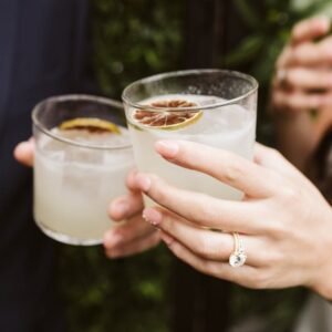 Close-up of a couple toasting with cocktails, highlighting a wedding ring during a celebration.
